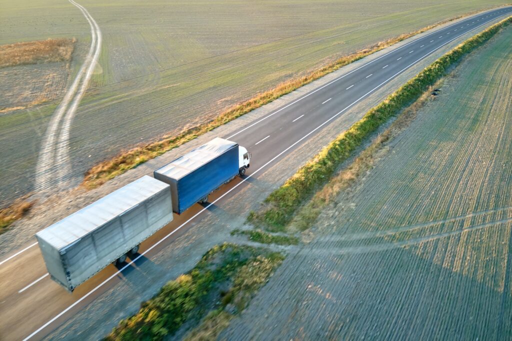 Aerial view of blurred fast moving semi-truck with cargo trailer driving on highway hauling goods in
